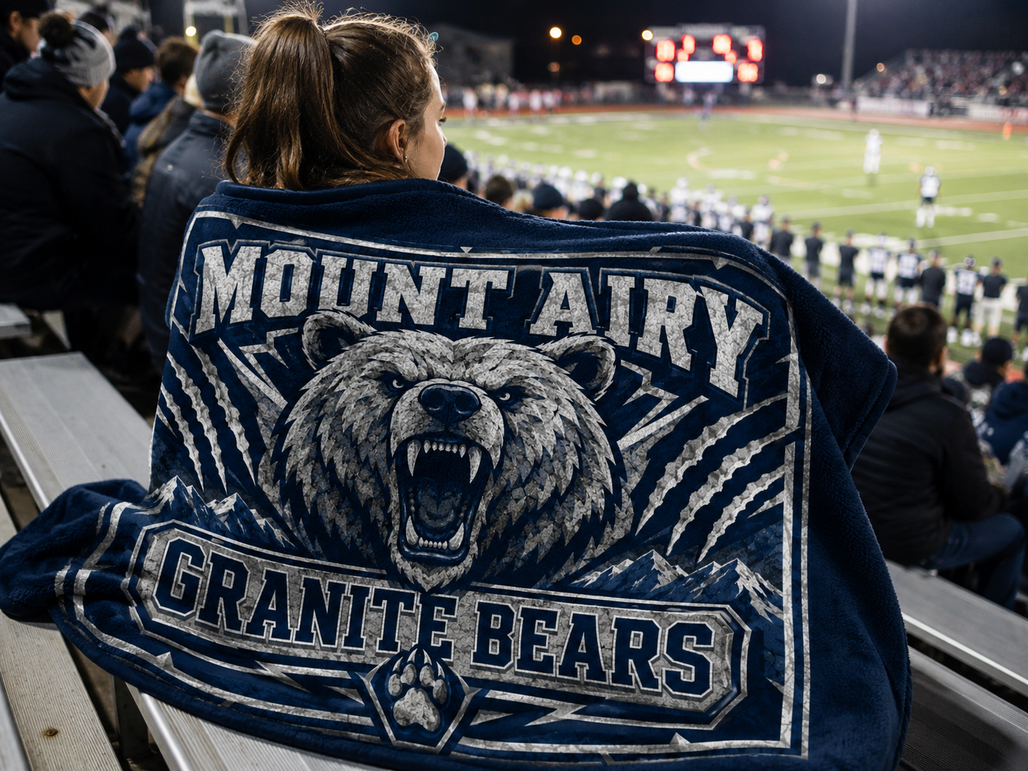 Fan wrapped in a custom fundraiser blanket printed with the Mount Airy Granite Bears logo at a football game