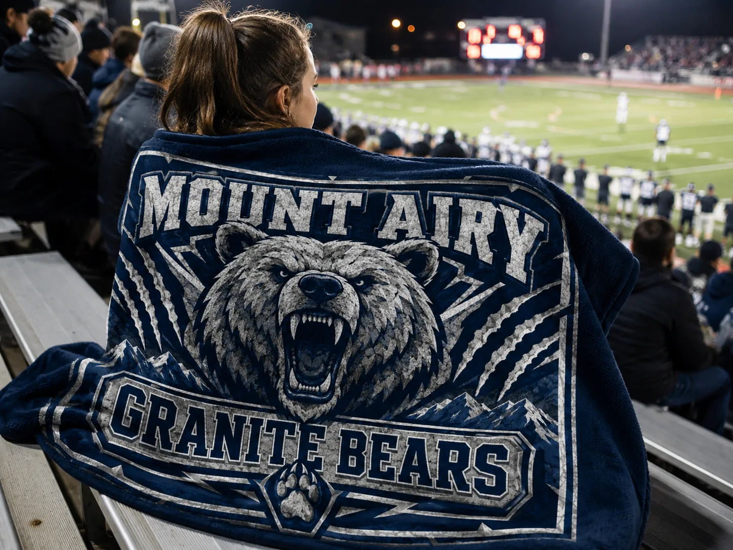 Fan wrapped in a custom fundraiser blanket printed with the Mount Airy Granite Bears logo at a football game